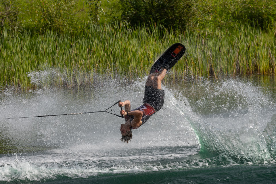 Trick skier inverted mid-flip above the wake